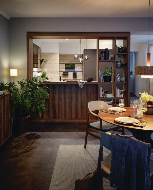 Kuchyně Schüller URBAN Arosa spojuje prostor pro vaření, bydlení a práci. Vycizelované policové skříně v jemném dřevěném vzhledu a kuchyňský pult rozdělují jednotlivé zóny.